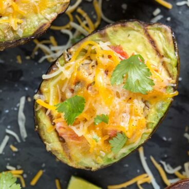 Half of avocado, grilled, with melted cheese, tomato, and cilantro on top