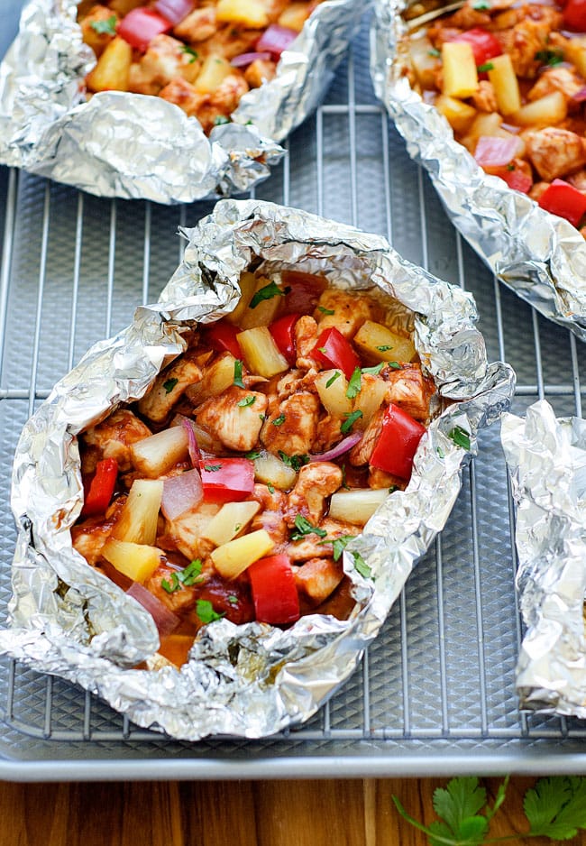 Foil packets with pineapple, chicken and peppers in them. A silver sheet pan and wire rack.