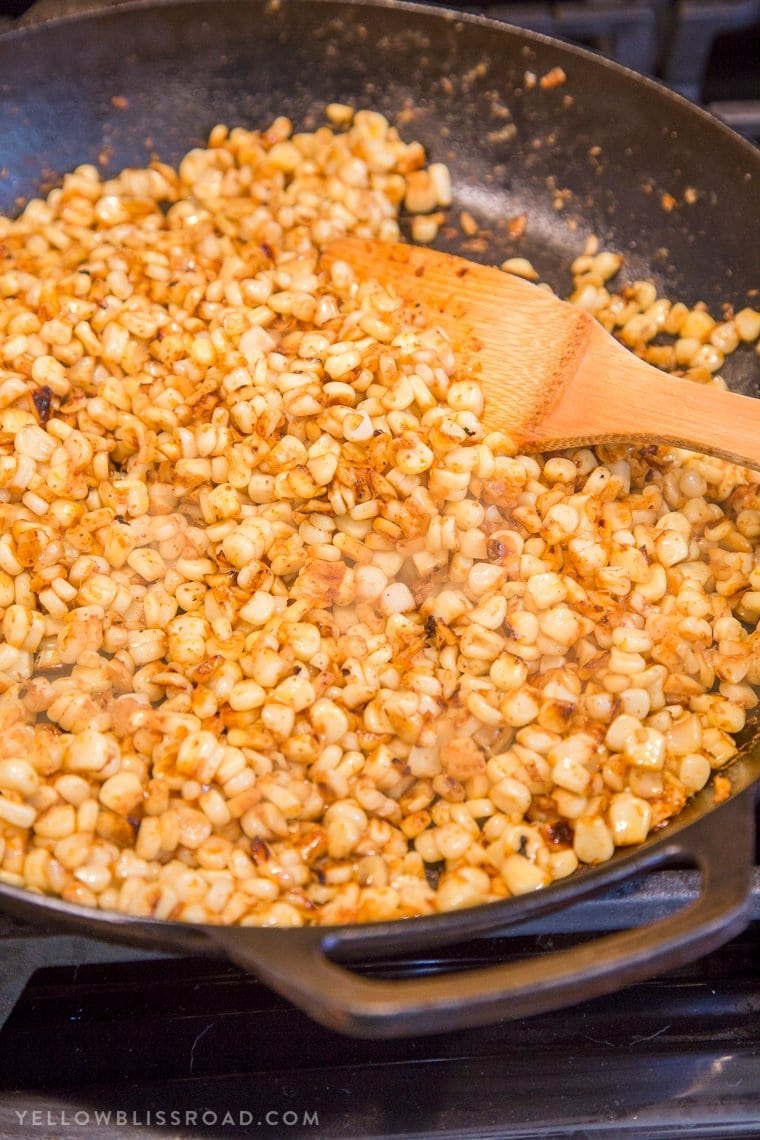 Corn kernels cooking in a large cast iron skillet