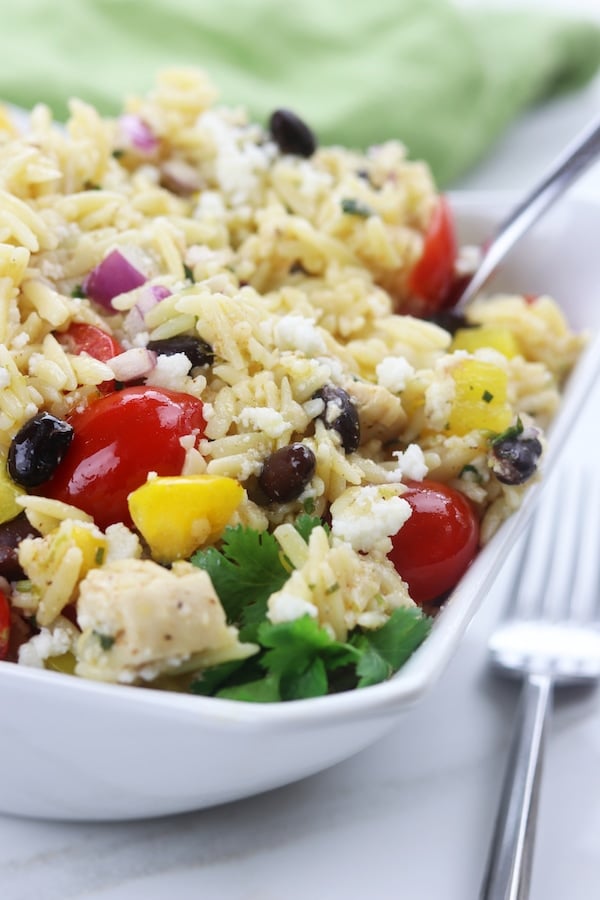 orzo, tomatoes, black beans and parsley in a small white dish with a fork.