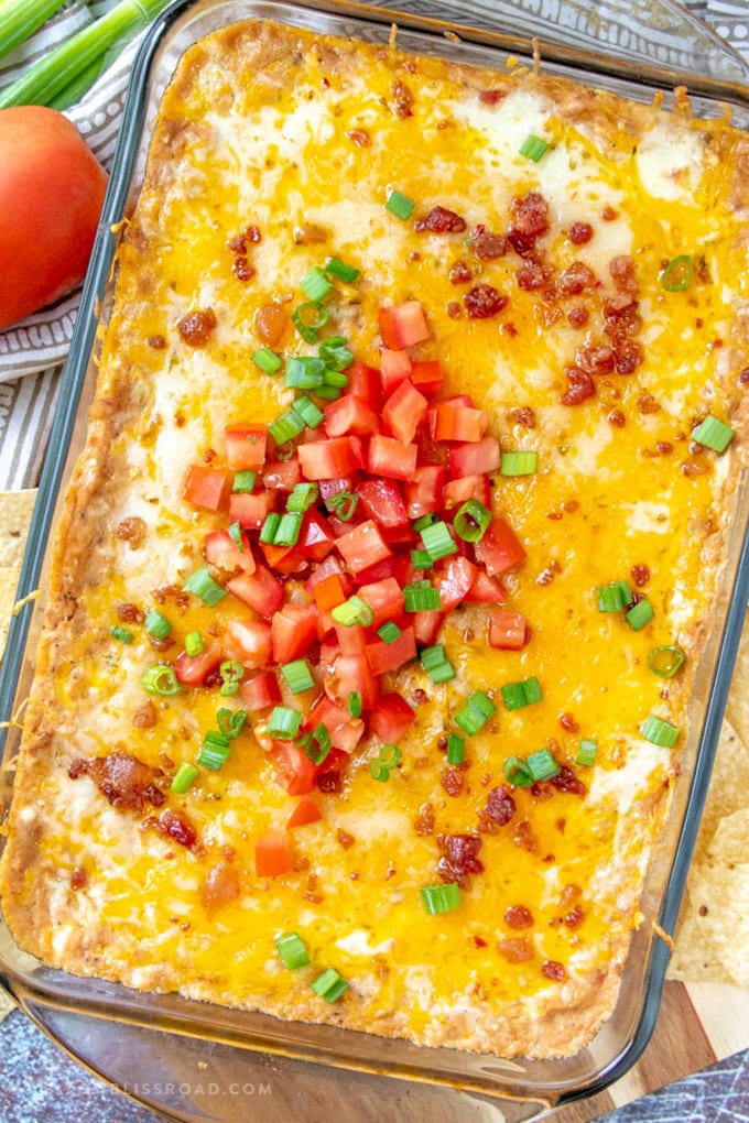 This Creamy Cheesy Refried Bean Bean Dip Recipe is highly addictive, intensely flavorful and sure to be your new favorite appetizer! Hot baked refried bean dip with tomatoes and onions.