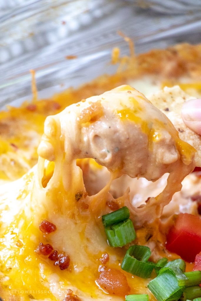 This Creamy Cheesy Refried Bean Bean Dip Recipe is highly addictive, intensely flavorful and sure to be your new favorite appetizer! Refried bean dip with cheese pulling up on a tortilla chip.