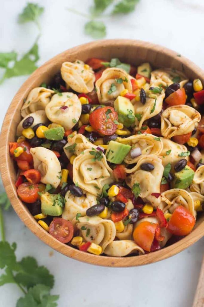 a wood bowl with tortellini, black beans, corn and tomatoes