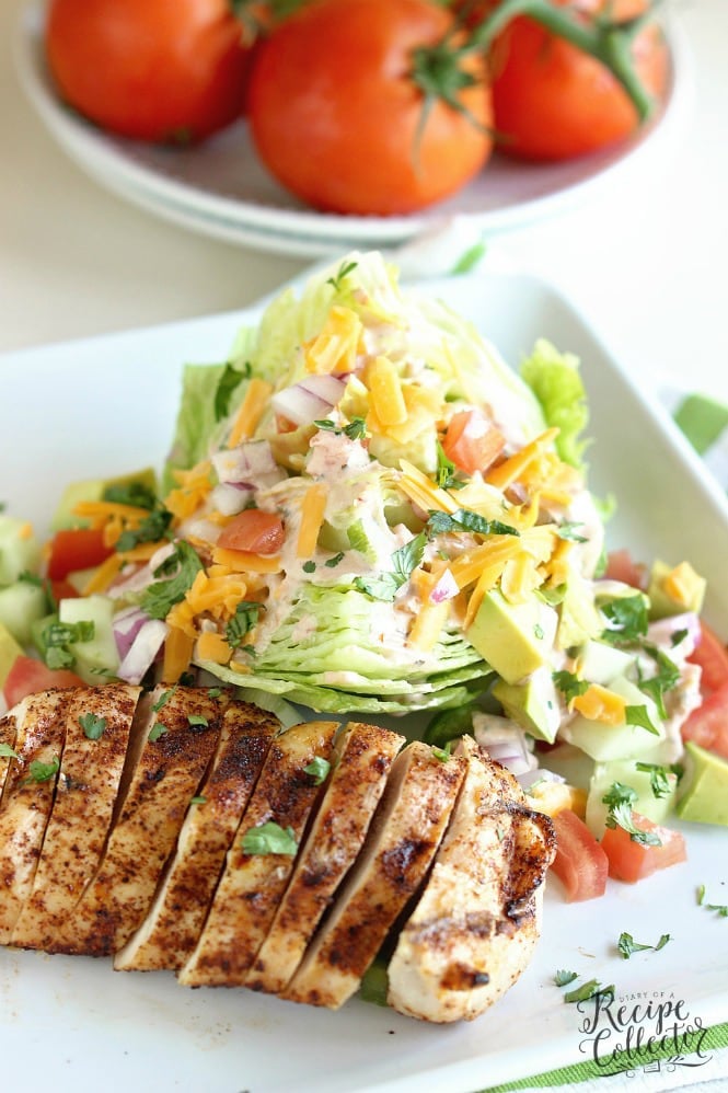 a white plate with sliced chicken and an iceber wedge salad with cheese and tomatoes and dressing. Ripe tomatoes on a stack of 2 plates.