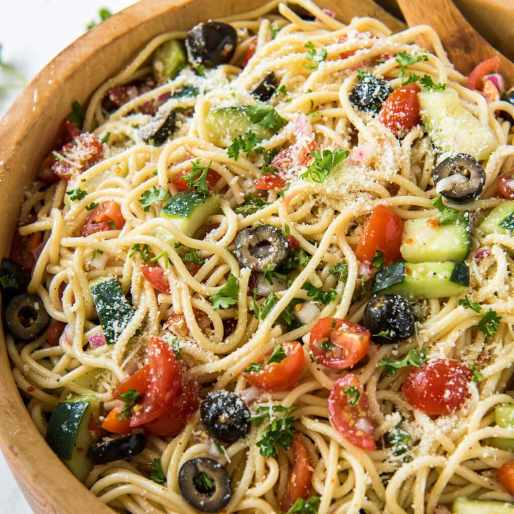 A bowl of spaghetti, olives, and tomatoes.