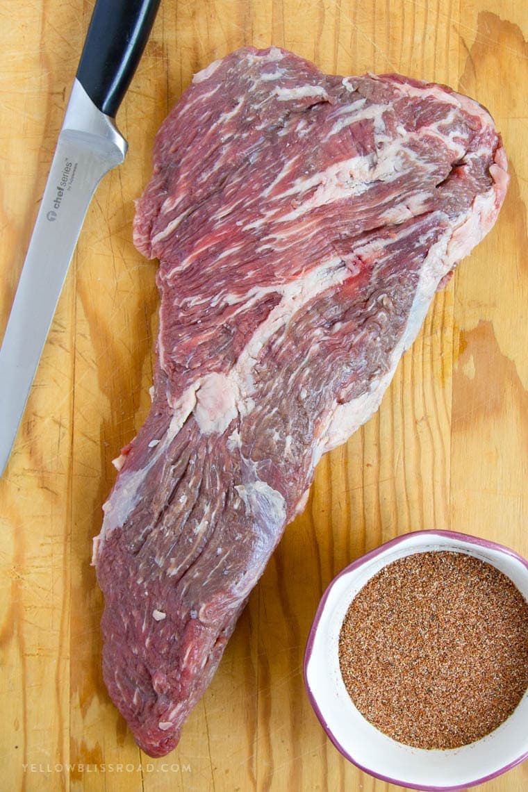 a raw whole tri tip, spices in a white dish, a knife