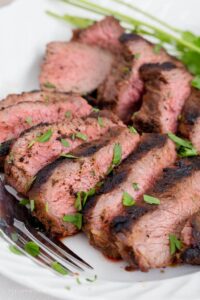 Grilled tri tip sliced, on a plate with a fork and parsley.