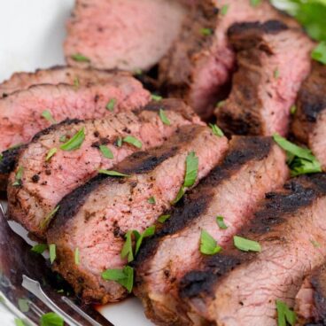 Grilled tri tip sliced, on a plate with a fork and parsley.