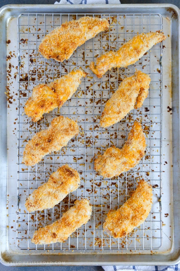 A baking sheet with a wire rack with breaded chicken tenders on top