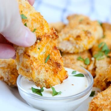 A close up of breaded chicken tenders dipping into ranch