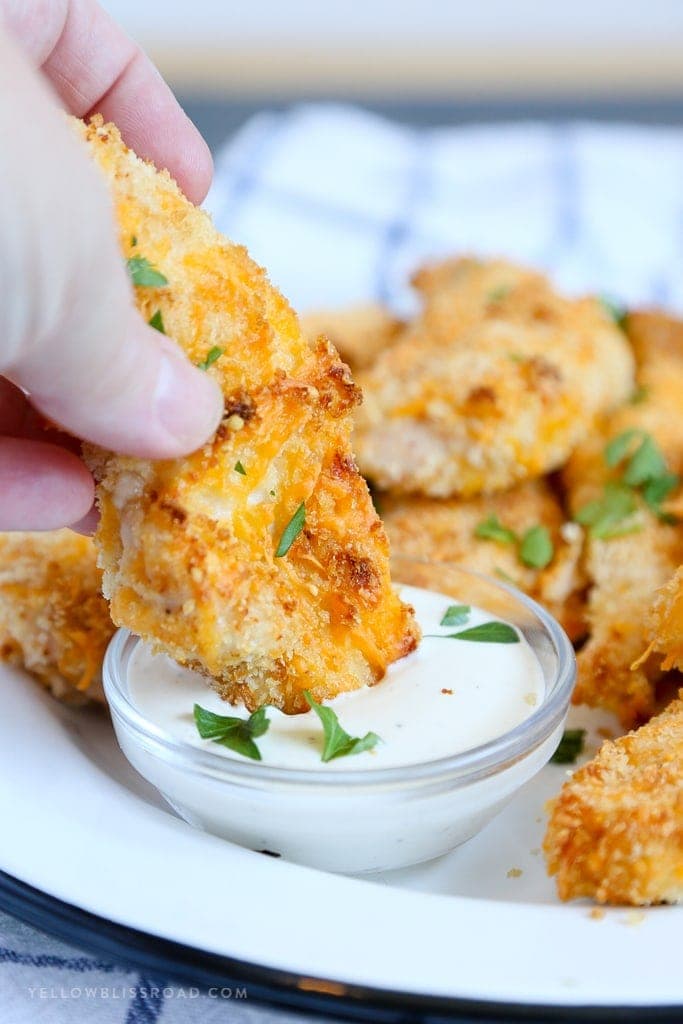 A close up of breaded chicken tenders dipping into ranch