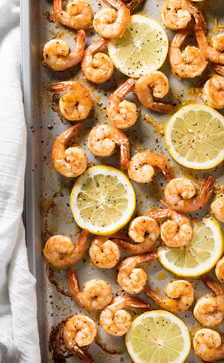 Half of a sheet pan with many shrimp with lemon pepper and lemon slices