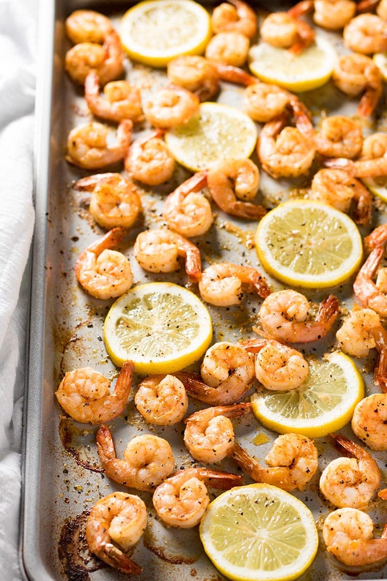 Close up view of a sheet pan full of lemon pepper shrimp with sliced lemons