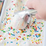 Ice cream with colorful sprinkles being scooped by hand.