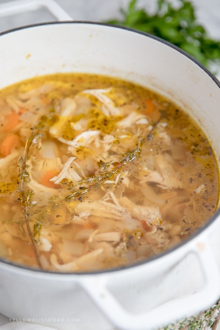 chicken broth in a large pot filled with chicken and vegetables with thyme leaves on top