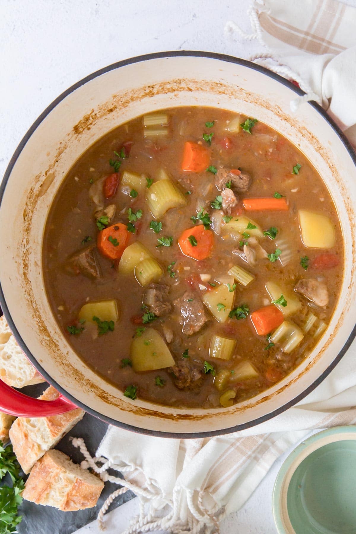 dutch oven pot, beef stew, parsley, bread, white towel