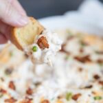 hand holding a piece of crostini with creamy dip and bacon on it.