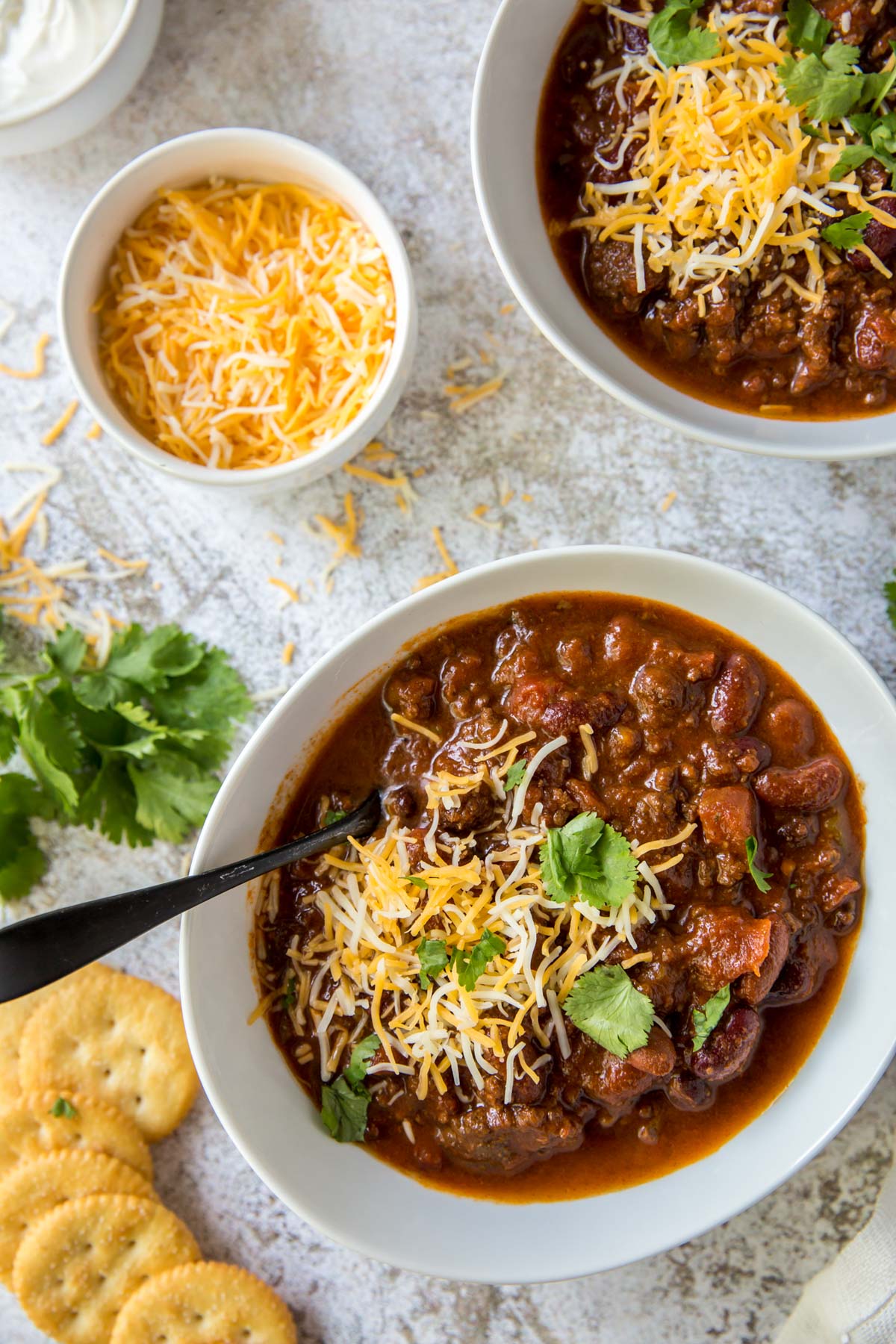 white bowls, chili, cheese, crackers, spoons, cilantro