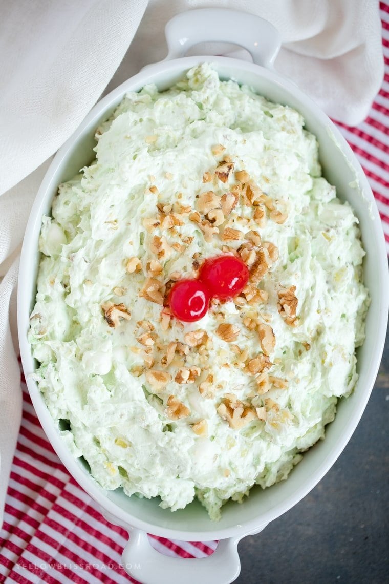 An overhead image of a dish filled with pistachio fluff salad with cherries and walnuts