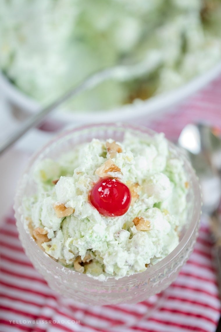 A small dish filled with pistachio salad and topped with a cherry