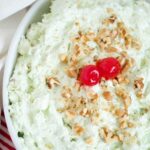 A bowl of pistachio fluff salad with maraschino cherries on top