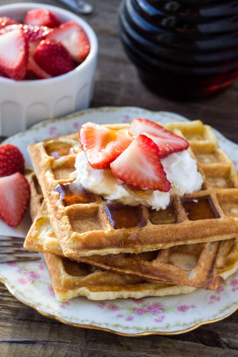 stack of waffles with whipped cream, syrup and strawberries