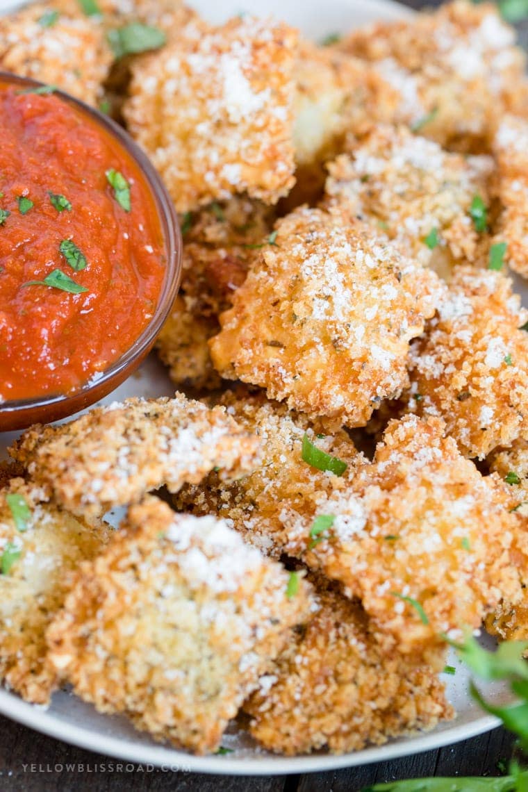 A plate full of fried ravioli and a bowl of marinara.