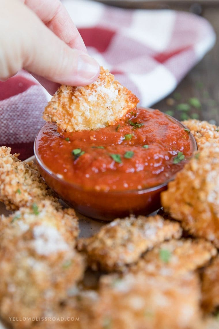 A hand holding one Fried Ravioli and dipping it in marinara.