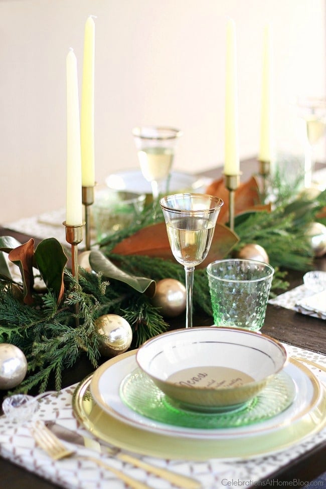 A decorated table with wine glasses, dishes, greenery, and candles