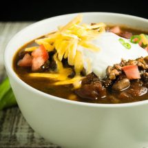 Healthy Turkey chili ready to eat in a white bowl topped with sour cream, cheese and tomatoes.