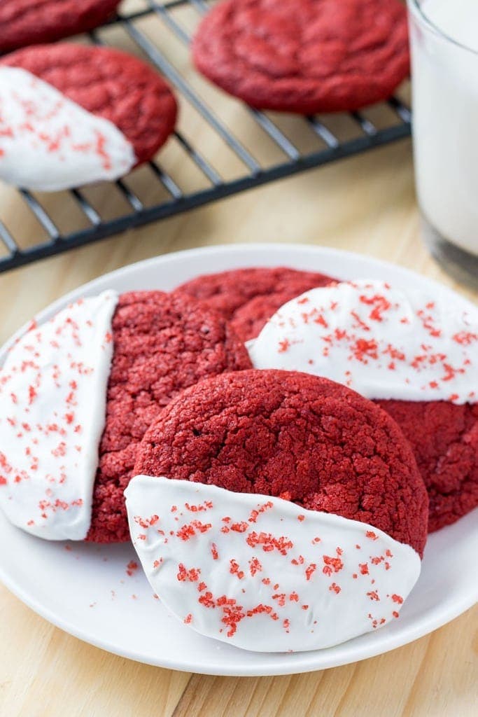 These red velvet cookies are soft, chewy & dipped in white chocolate. Pictured with a glass of milk. 