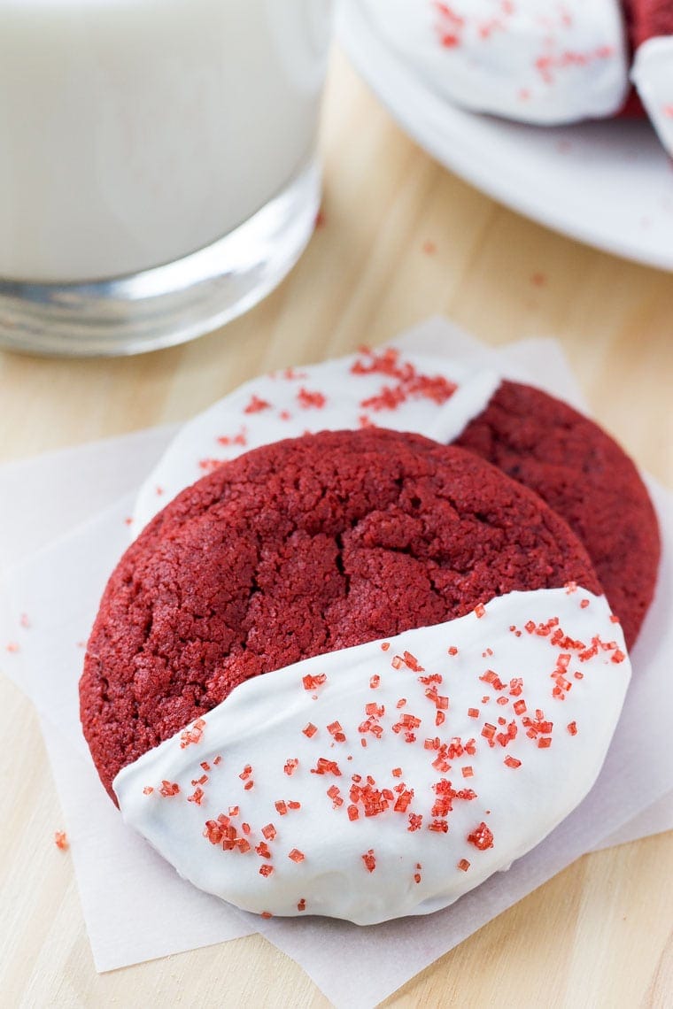 Two soft and chewy red velvet cookies dipped in chocolate and decorated with sprinkles. 