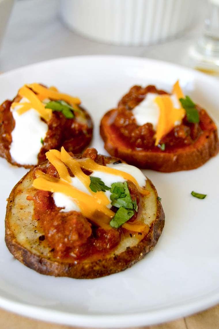 Chili on top of Sweet potato Slices on a plate topped with Cheese and Sour Cream