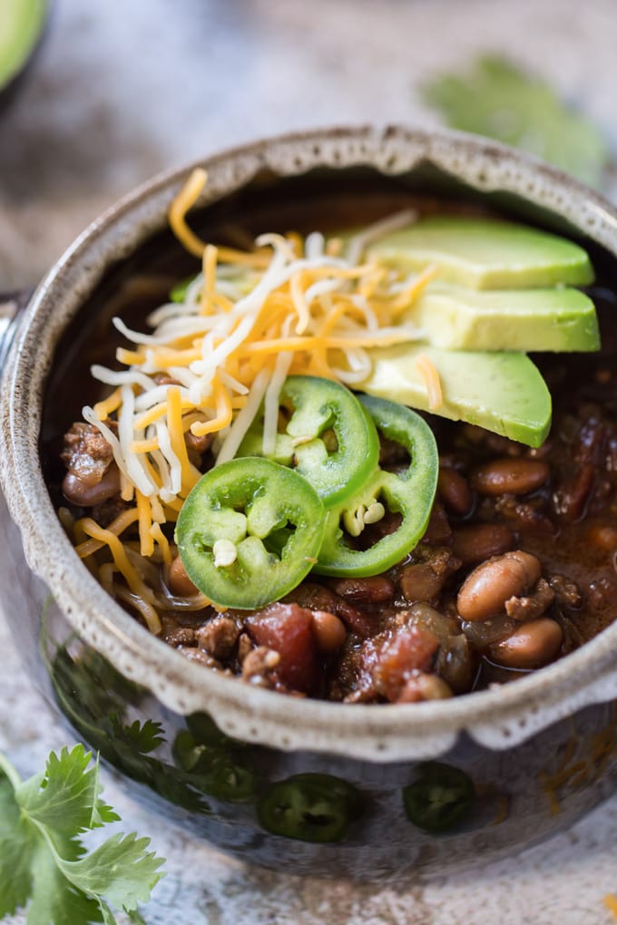 a bowl of turkey chili topped with cheese, jalapenos and avocado