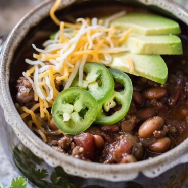 A bowl of chili with avocado slices, cheese, and jalapenos