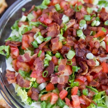 BLT dip in a glass pie dish with lettuce, green onions and bacon and tomatoes