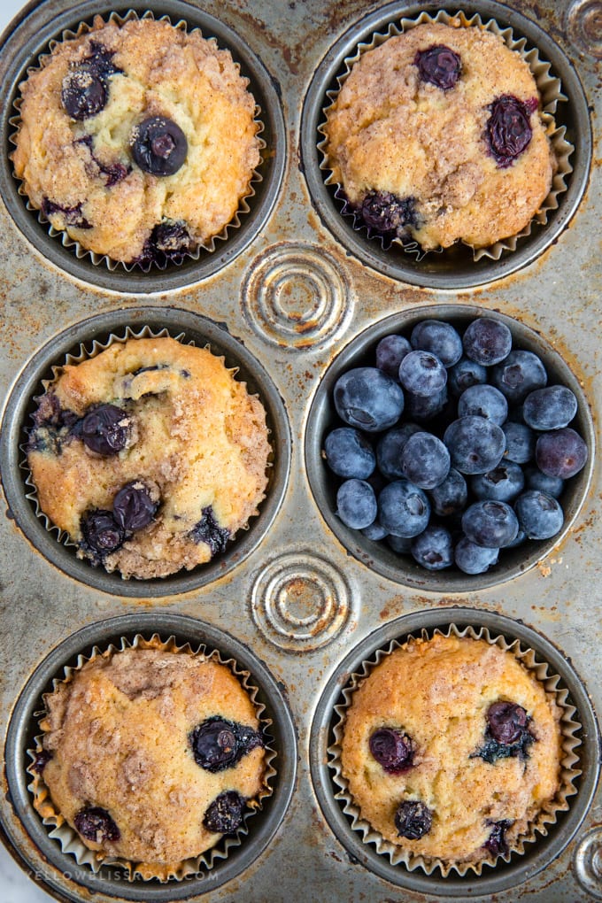 Blueberry Sour Cream Coffee Cake Muffins close up in a muffin tin full of blueberries