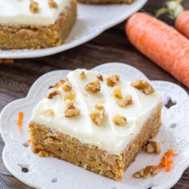 A slice of moist, chewy carrot cake bars with cream cheese frosting and chopped walnuts.