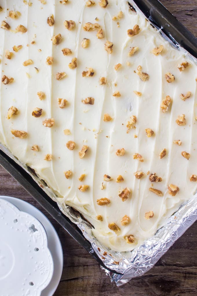 Carrot Cake Bars with Cream Cheese Frosting are chewy, dense, moist, and filled with all the flavor of your favorite carrot cake. Then they're topped with cream cheese frosting and a few chopped walnuts for the best easy dessert recipe! Overhead shot of a tray of carrot cake bars with cream cheese frosting.