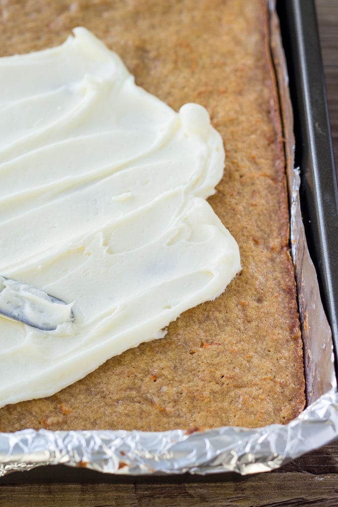 Carrot Cake Bars with Cream Cheese Frosting are chewy, dense, moist, and filled with all the flavor of your favorite carrot cake. Then they're topped with cream cheese frosting and a few chopped walnuts for the best easy dessert recipe! A tray of carrot cake bars being frosted with cream cheese buttercream.