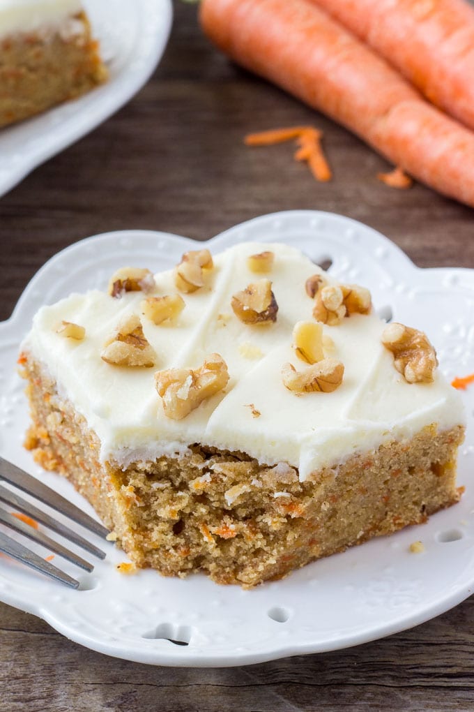 A slice of carrot cake bars with cream cheese frosting with a bite taken out. 