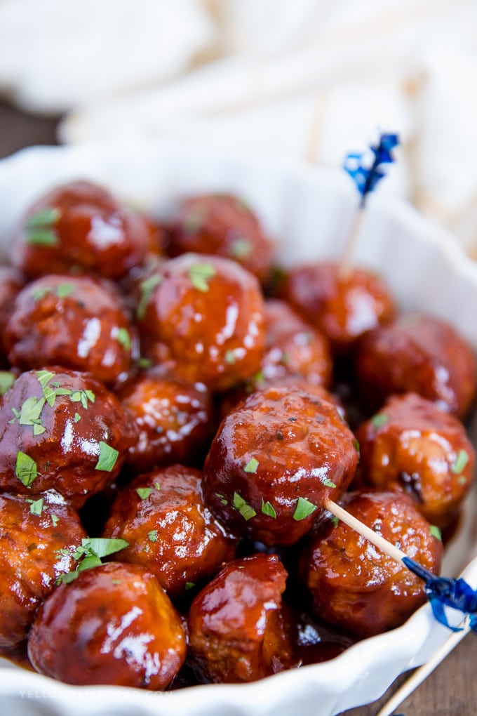 a side view of a stack of meatballs coated in grape jelly and barbecue sauce with toothpicks.