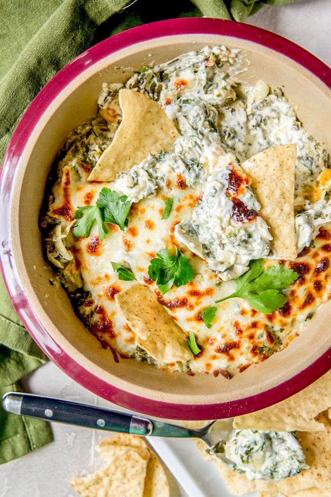 An overhead shot of a dish of spinach artichoke with tortilla chips dipped in.