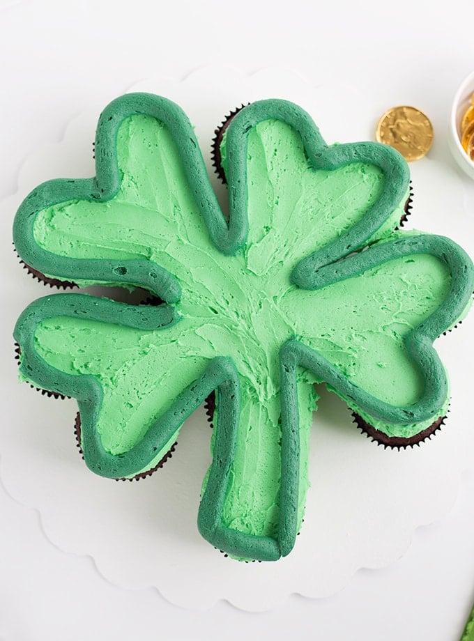 Green frosted cupcakes on a white cake board in the shape of a shamrock with a dark green outlining the shamrock