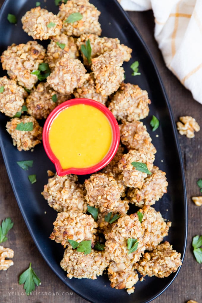 Walnut Crusted Baked Chicken Nuggets: tender, juicy chicken coated in crunchy walnuts and seasonings. Easy appetizer or dinner. #ad #californiawalnuts Overhead shot of Walnut Crusted Baked Chicken Nuggets on a platter with honey mustard dipping sauce
