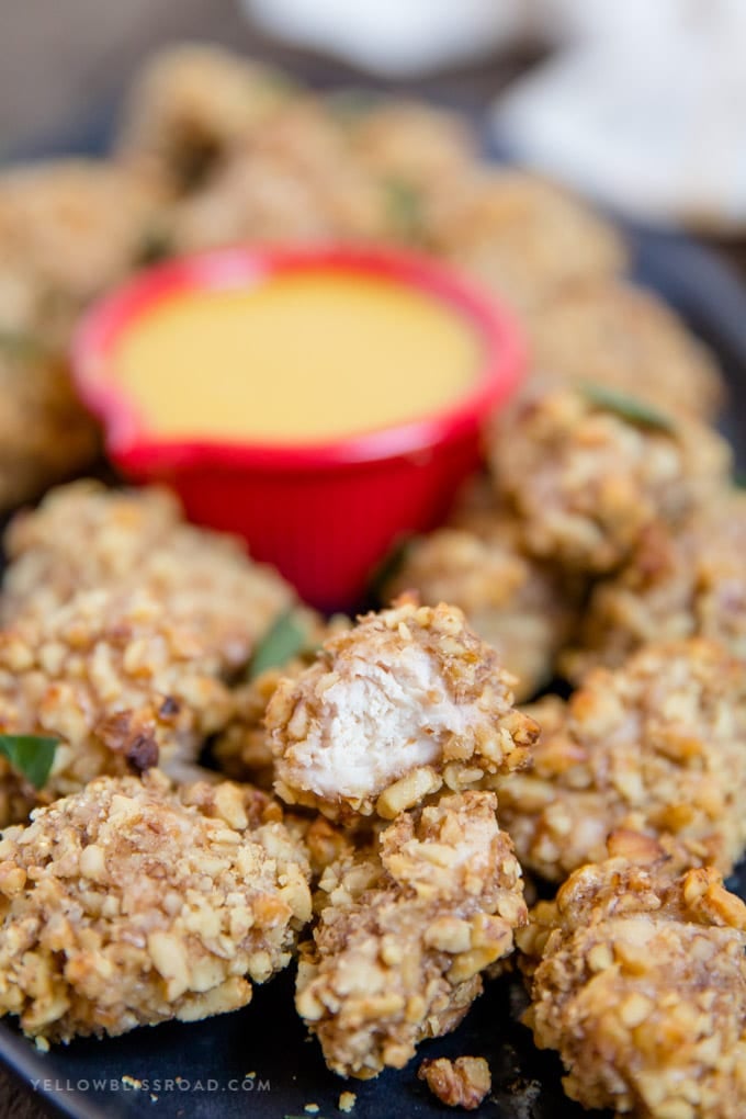 Walnut Crusted Baked Chicken Nuggets: tender, juicy chicken coated in crunchy walnuts and seasonings. Easy appetizer or dinner. #ad #californiawalnuts Walnut Crusted Baked Chicken Nuggets stacked with a bite taken out of it