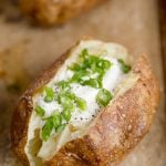 A close up of baked potato with sour cream and chives on top