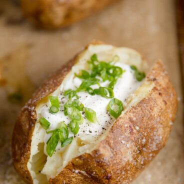 A close up of baked potato with sour cream and chives on top