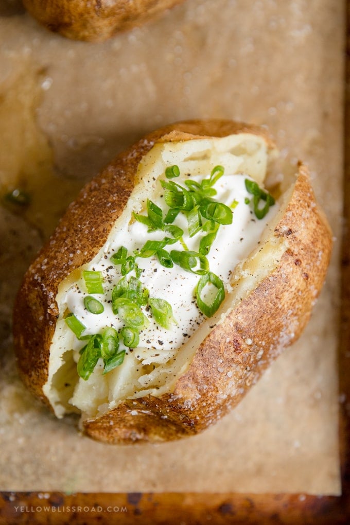 A close up of a baked potato with sour cream and chives on top