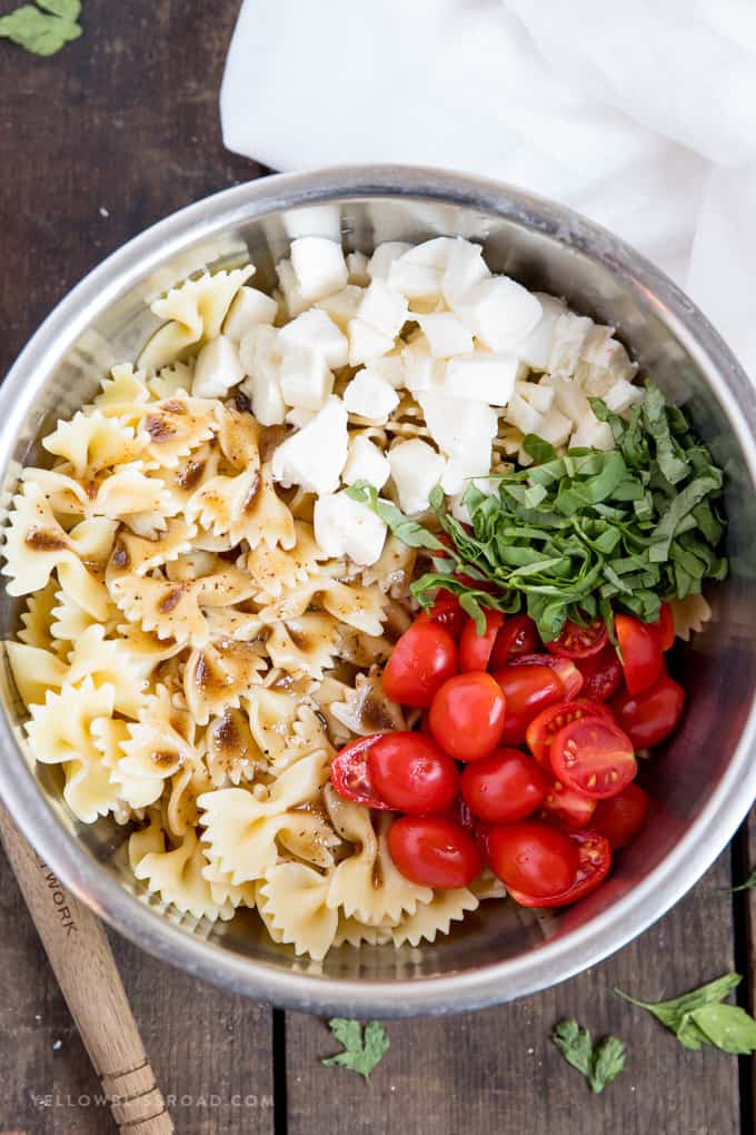 Ingredients for making Caprese Pasta Salad in a bowl with tomatoes, mozzarella cheese, basil and pasta